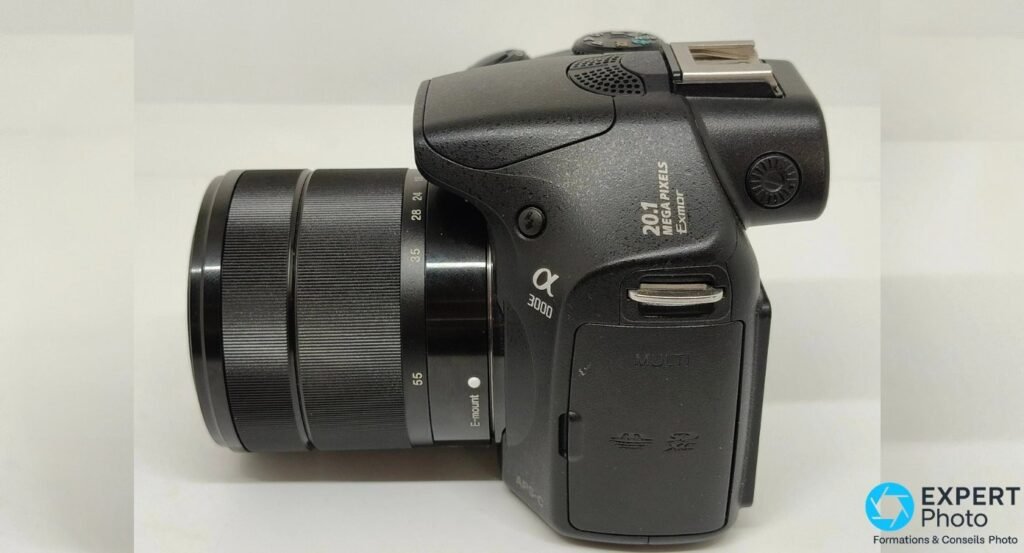 Profil gauche du Sony Alpha 3000 avec objectif monté, marquages 20.1 MEGAPIXELS Exmor, APS-C et E-mount visibles. 