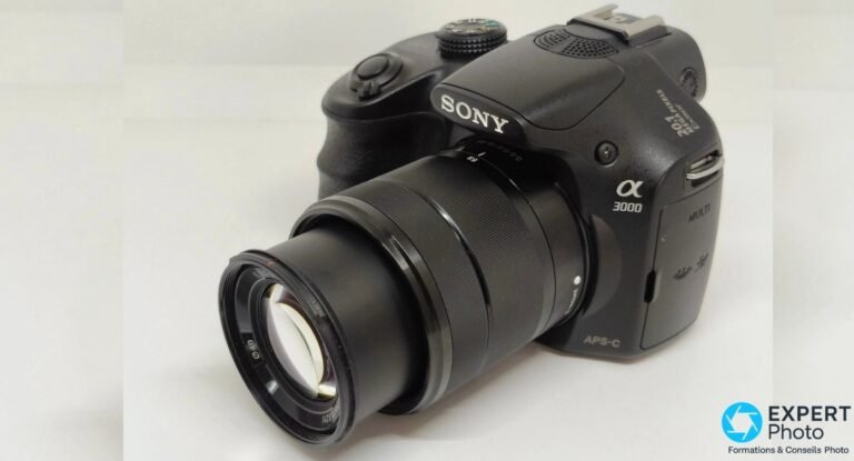 Sony Alpha 3000 vu de trois quarts avant, objectif kit Sony E 18-55 mm OSS déployé en position téléobjectif sur fond clair.
