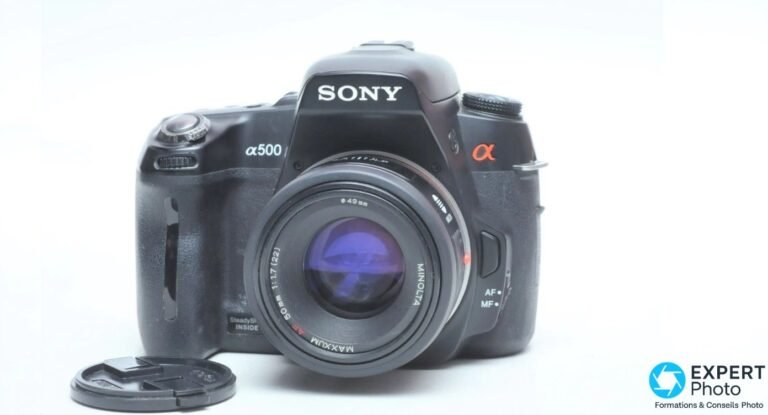 Sony Alpha 500 (DSLR-A500) : que vaut ce reflex APS-C d’occasion en 2026 ? Boîtier Sony Alpha 500 vu de face trois-quarts avec objectif Minolta AF 50 mm f/1.7 monté, bouchon posé devant.