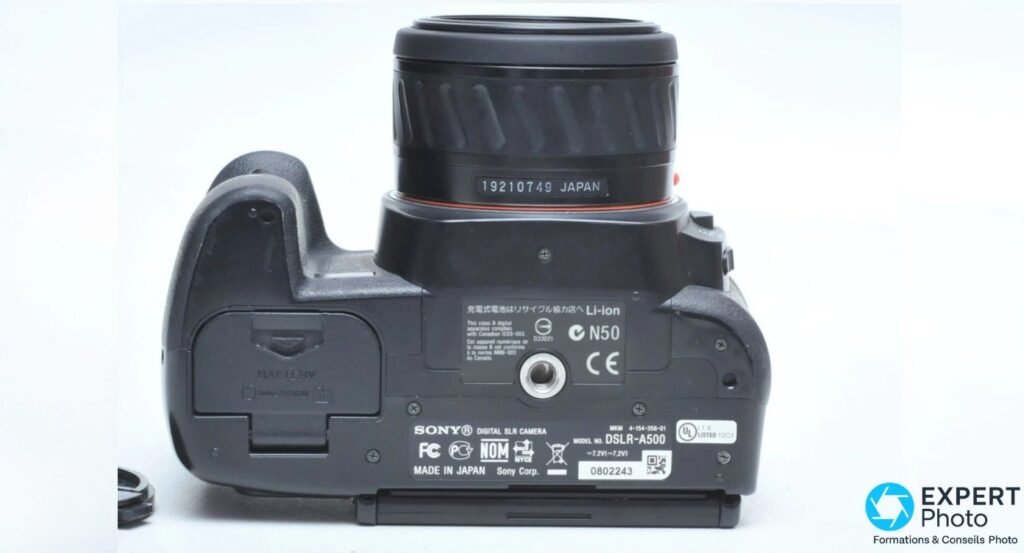 Plaque inférieure du Sony DSLR-A500 montrant le modèle, le pas de vis trépied et le compartiment batterie.