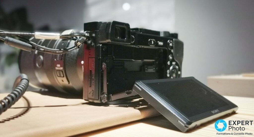 Vue arrière du Sony Alpha 6100, écran inclinable rabattu vers le bas, sangle attachée et objectif zoom gris monté. 