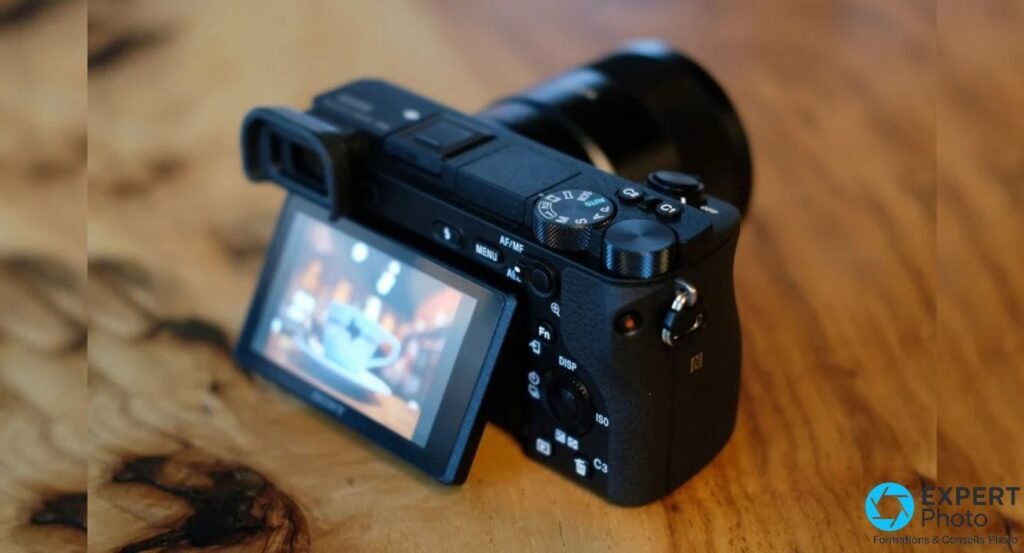 Sony Alpha 6500 vu de trois-quarts arrière, écran inclinable déployé, molette de mode et boutons MENU AF/MF AEL visibles. 