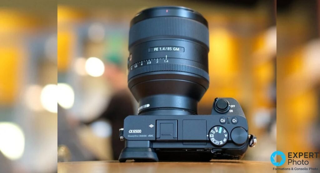 Sony Alpha 6500 vu du dessus avec un objectif Sony FE 85 mm f/1.4 GM monté, molette de mode et boutons C1 C2 visibles.