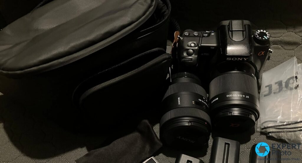 Sony Alpha A700 avec objectif Sony DT 55-200 et second zoom Sony, sac photo noir, sachet JJC, disposés sur surface textile sombre