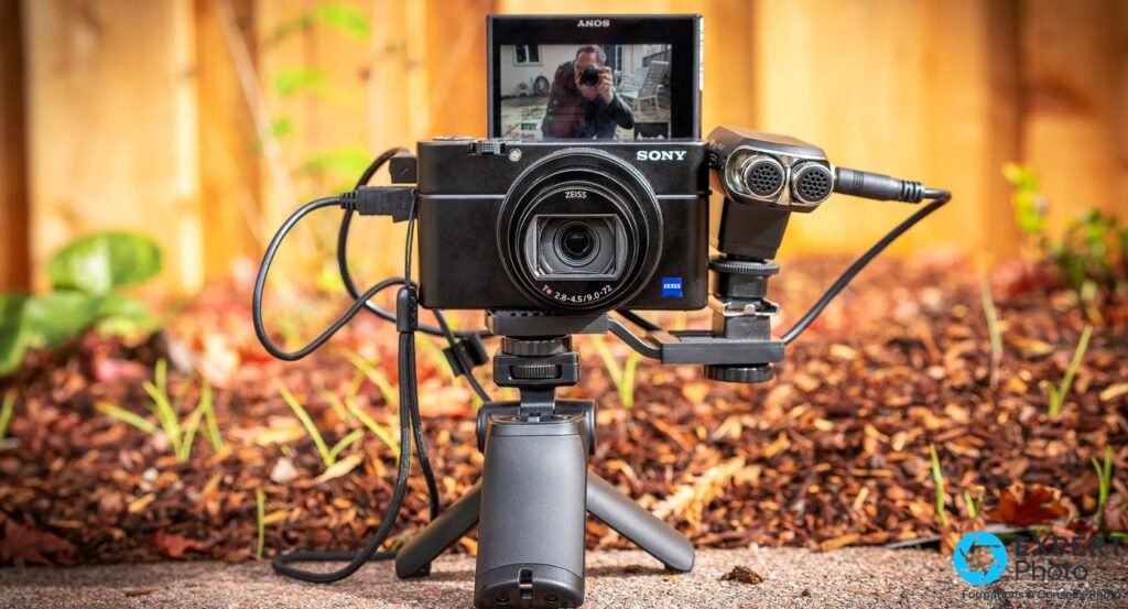 Sony RX100 VII de face sur grip compact, écran vlog retourné affichant un selfie, micro externe à droite, fond extérieur