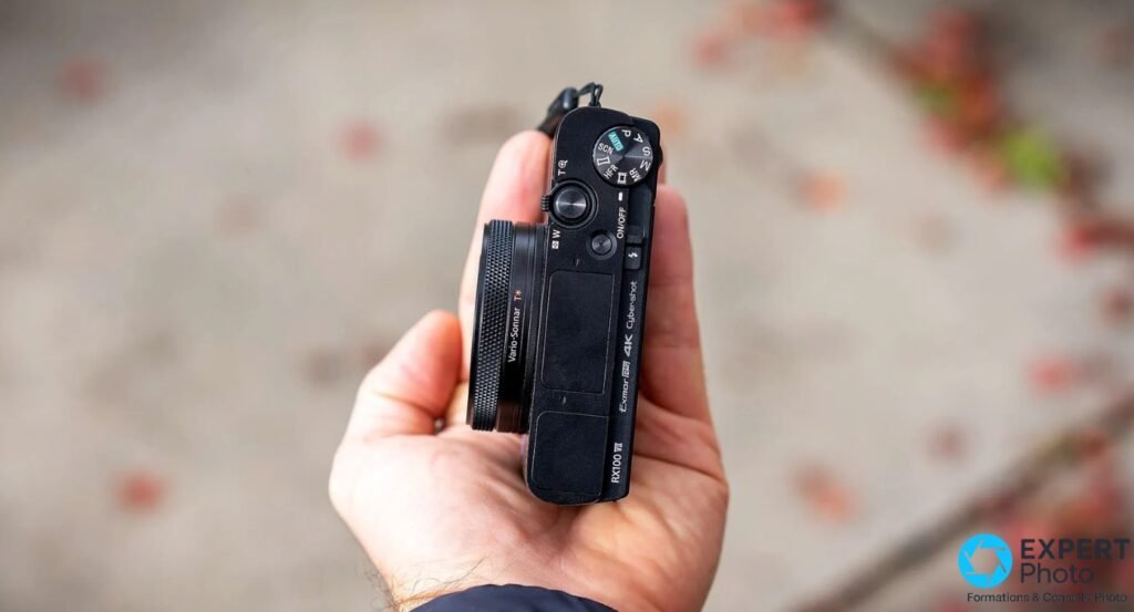 Sony RX100 VII tenu en main, profil droit, inscription RX100 VII et Vario-Sonnar T* lisibles, zoom rétracté, fond neutre 