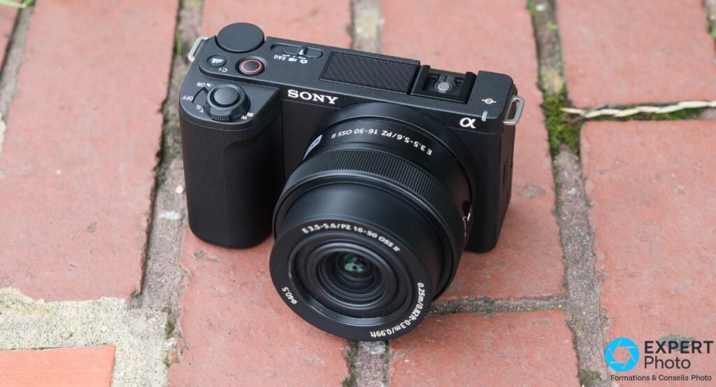 Sony ZV-E10 II noir de trois quarts avant, objectif PZ 16-50mm vers l'avant, posé sur des briques rouges