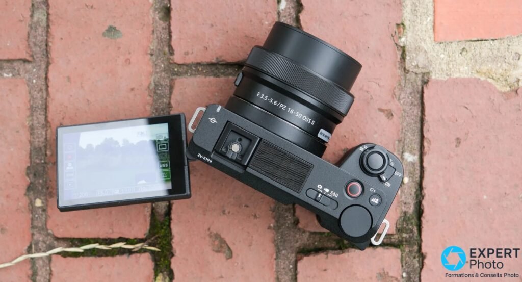 Sony ZV-E10 II noir de dessus, ecran orientable deploye affichant l'interface, objectif PZ 16-50mm, sur briques