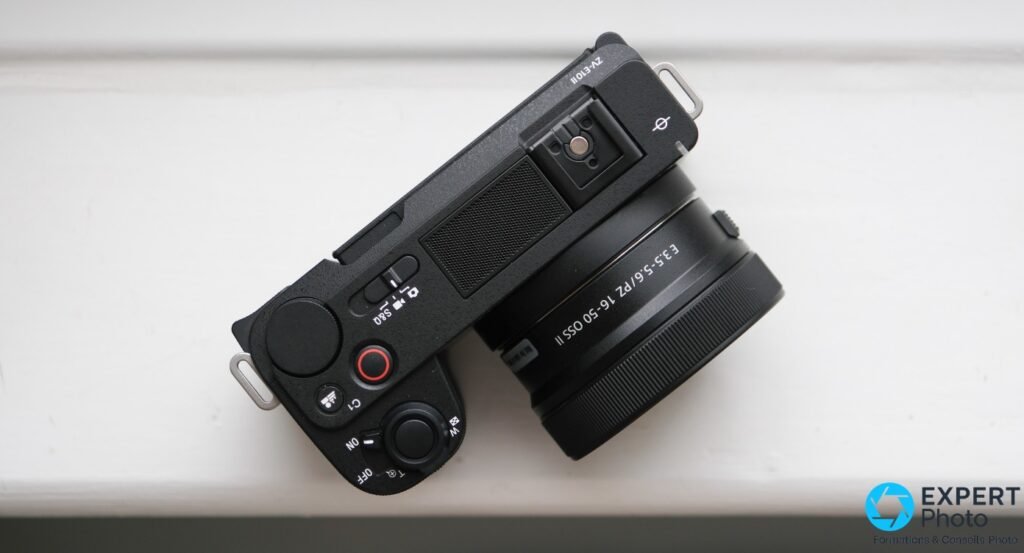 Sony ZV-E10 II noir vu de dessus, objectif PZ 16-50mm monte, ecran ferme, pose sur une surface blanche
