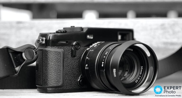 7Artisans 35mm f/0.95 : avis, ouverture réelle et alternatives 7Artisans 35mm f/0.95 avec pare-soleil monté sur boîtier compact noir, vue 3/4 avant, bague 35mm 1:0.95 lisible, photo N&B
