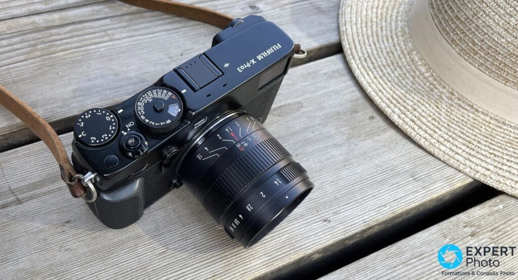 Fujifilm X-Pro3 en plongée inclinée, objectif 7Artisans 55mm f/1.4 monté, bague MAP et molettes visibles, chapeau paille