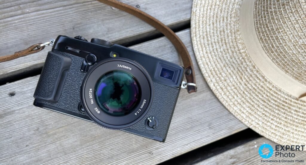 Boîtier hybride noir avec objectif 7Artisans 55mm f/1.4 (Φ52 No.20724) posé sur lattes bois, chapeau paille à droite