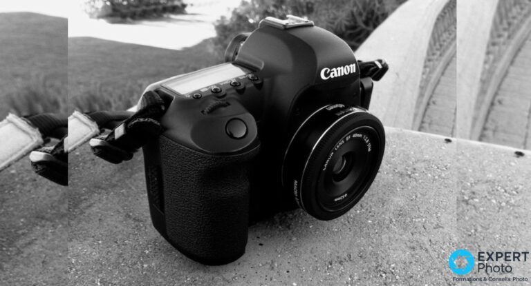 Reflex Canon noir avec objectif Canon EF 40mm f/2.8 STM monté, vue 3/4 avant, posé sur béton, noir et blanc