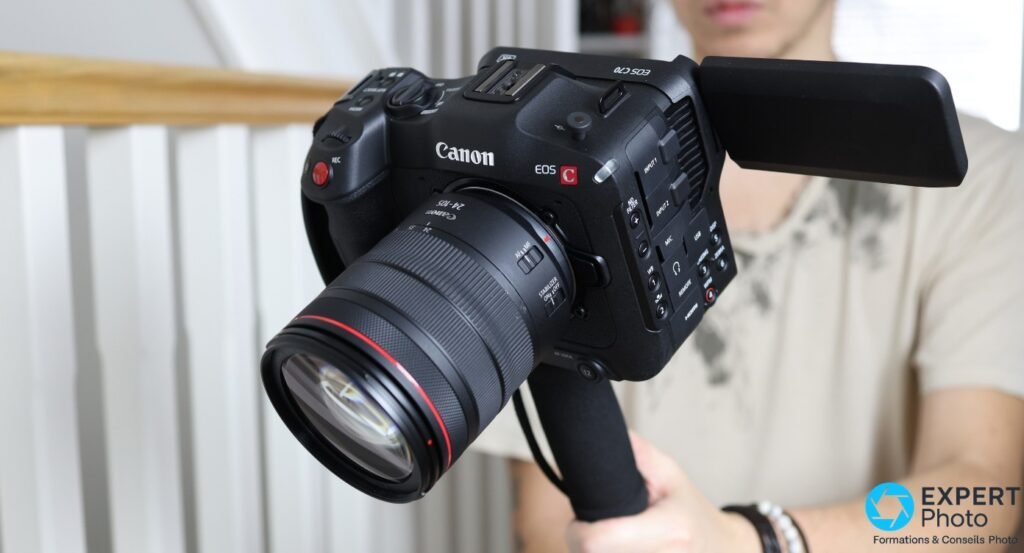Canon EOS C70 avec zoom RF 24-105mm à anneau rouge, écran orientable déployé latéralement, tenu en main, marquages EOS C70 visibles