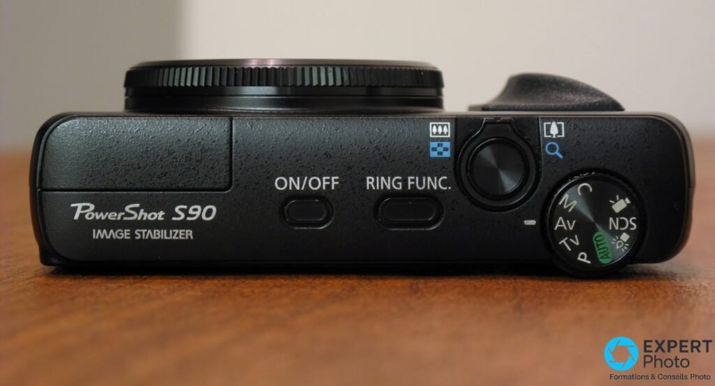 Canon PowerShot S90 vu du dessus posé, molette PASM avec positions M Av Tv P AUTO, boutons ON/OFF et RING FUNC. 