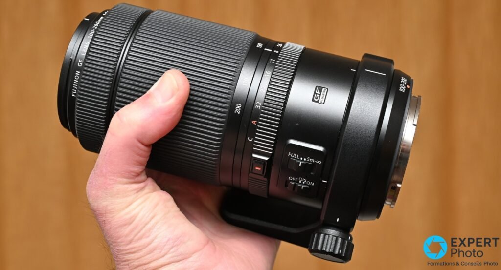 Objectif Fujinon GF 100-200mm tenu en main, profil droit incliné, bague de zoom avec graduations 100-200 et logo GF Fujinon sur le fût