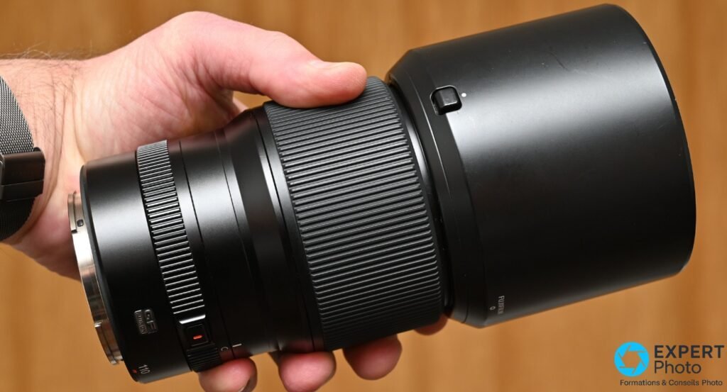 Objectif Fujinon GF 110mm f/2 R LM WR avec pare-soleil cylindrique noir monte, vue laterale, monture argentee visible