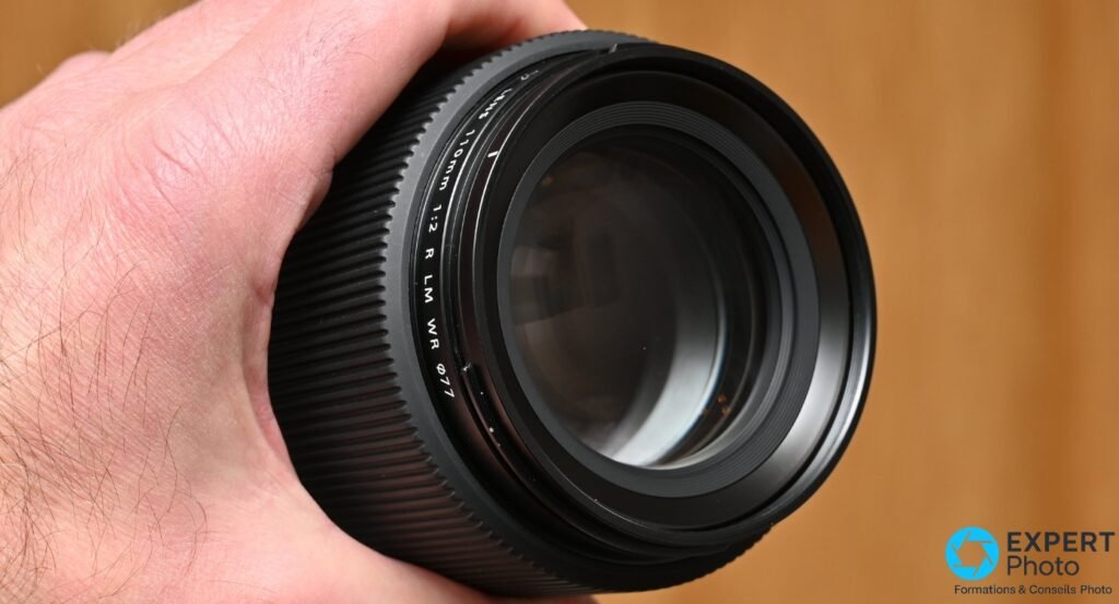 Vue de face de la lentille frontale du Fujinon GF 110mm f/2 R LM WR Ø77, reflet bleuté du traitement antireflet visible