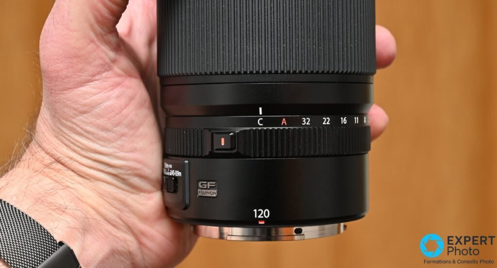 Objectif Fujifilm GF 120mm f/4 Macro monté sur un boîtier Fujifilm GFX, vue trois quarts avant, fond blanc 