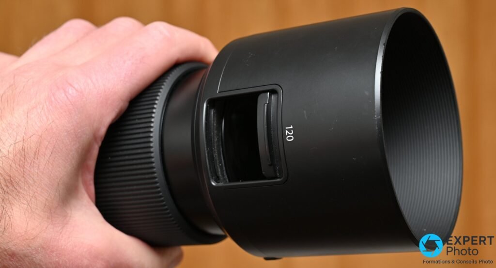 Objectif Fujifilm GF 120mm f/4 Macro monté sur un boîtier Fujifilm GFX, tenu à la main droite, vue trois quarts 