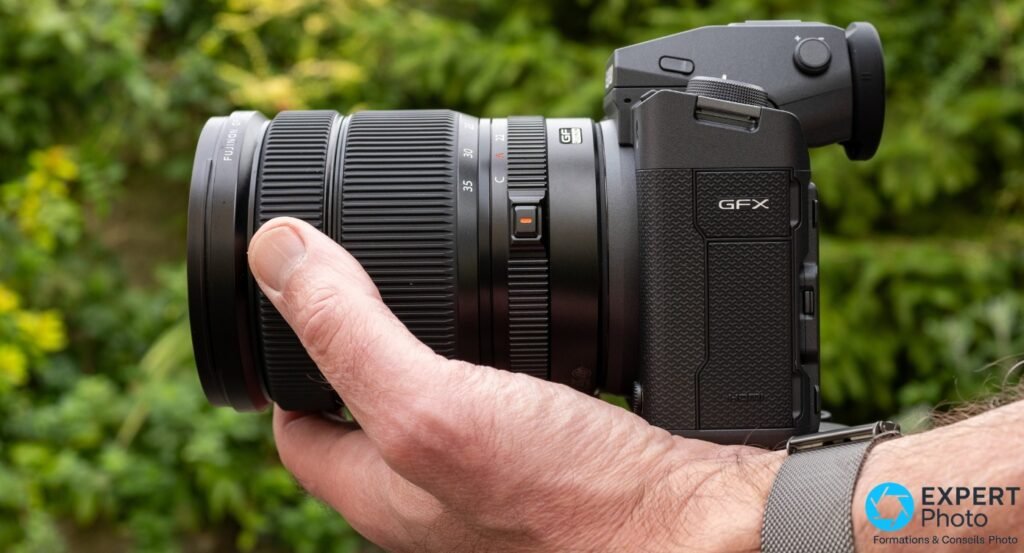Fujifilm GF 20-35mm f/4 R WR sur GFX, profil droit, inscription GFX, port HDMI et sangle photo grise au poignet visibles