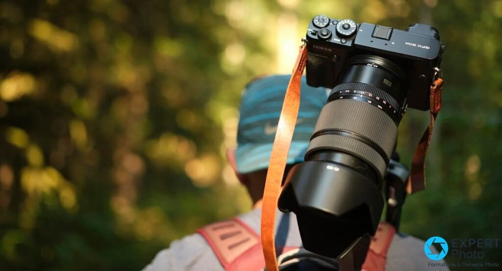 Fujifilm GF 45-100mm f/4 avec pare-soleil, monté sur GFX 50R, porté par un photographe de dos en extérieur, sangle cuir.