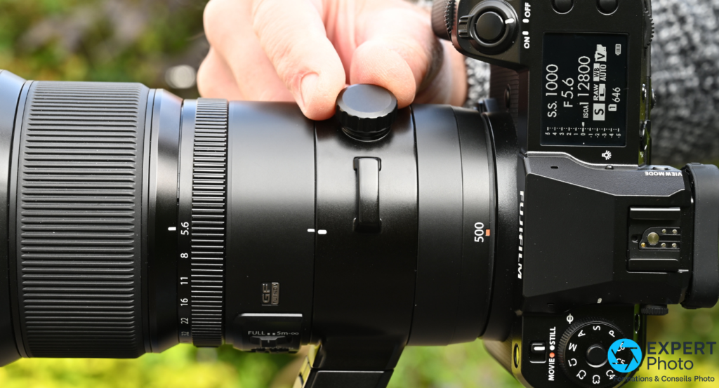  Fujifilm GF 500mm f/5.6 vue de dessus sur boîtier GFX, marquage 500 orange visible, écran de dessus allumé 