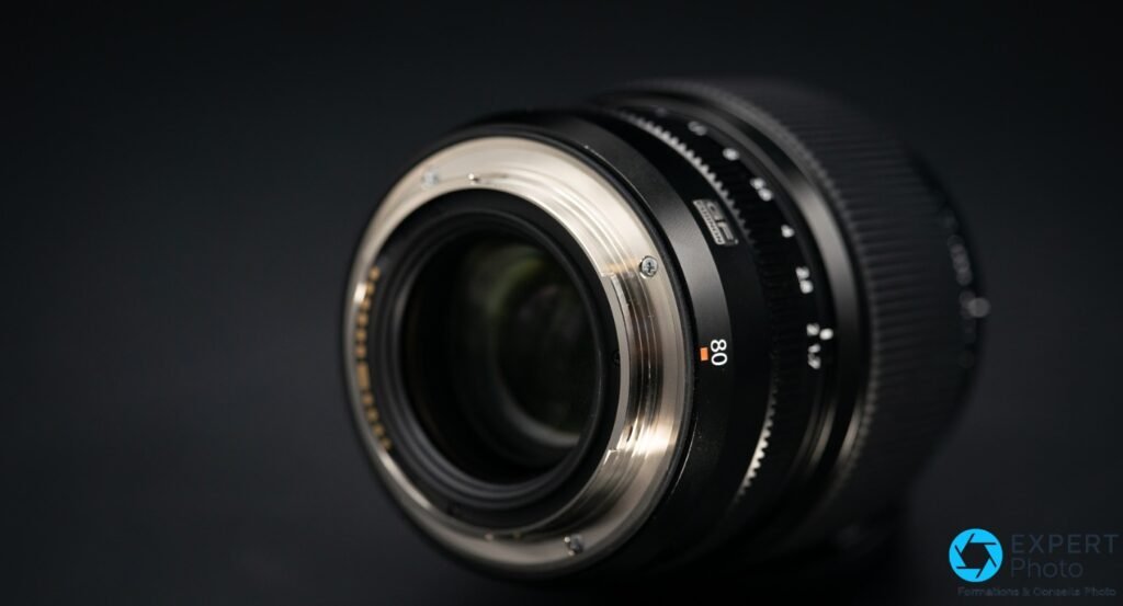 Fujifilm GF 80mm f/1.7 R WR, vue 3/4 arrière sur la monture argentée et les contacts dorés alignés, verre arrière visible
