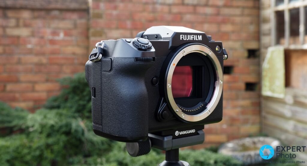 Fujifilm GFX 100S boîtier nu de face, monture G ouverte avec capteur rose visible, sur trépied Vanguard, fond brique flou