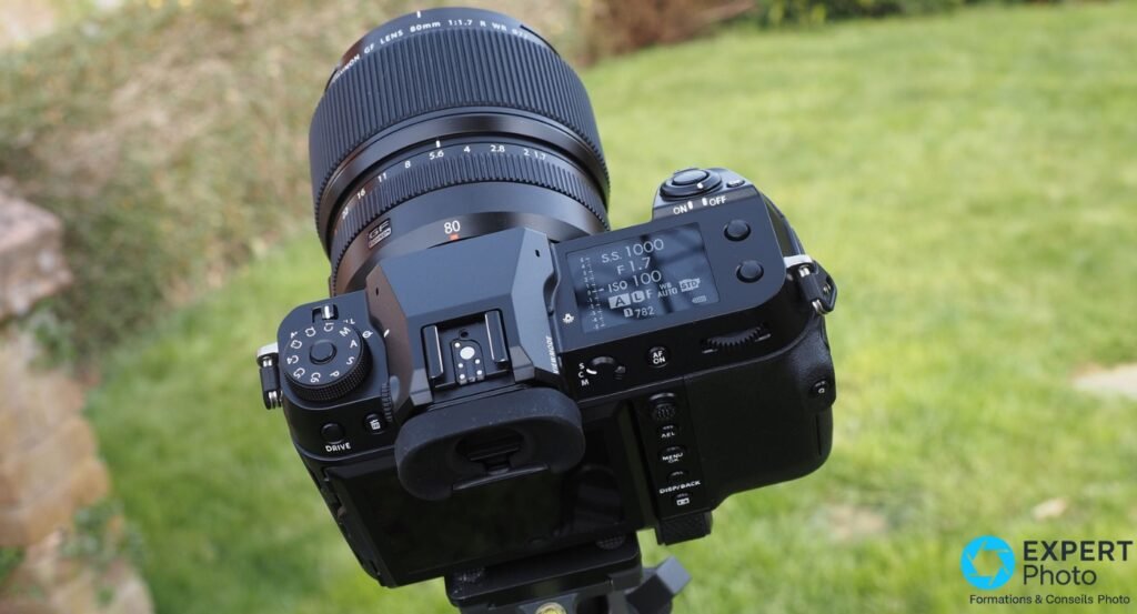  Fujifilm GFX 100S dessus avec écran LCD affichant SS 1000 F 1.7 ISO 100, bague objectif Fujinon GF 80mm visible