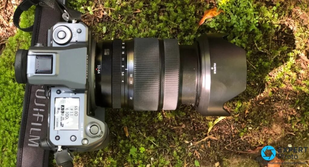 Fujifilm GFX 100 vu du dessus avec objectif GF 32-64 mm monté et pare-soleil, posé sur fond de végétation verte