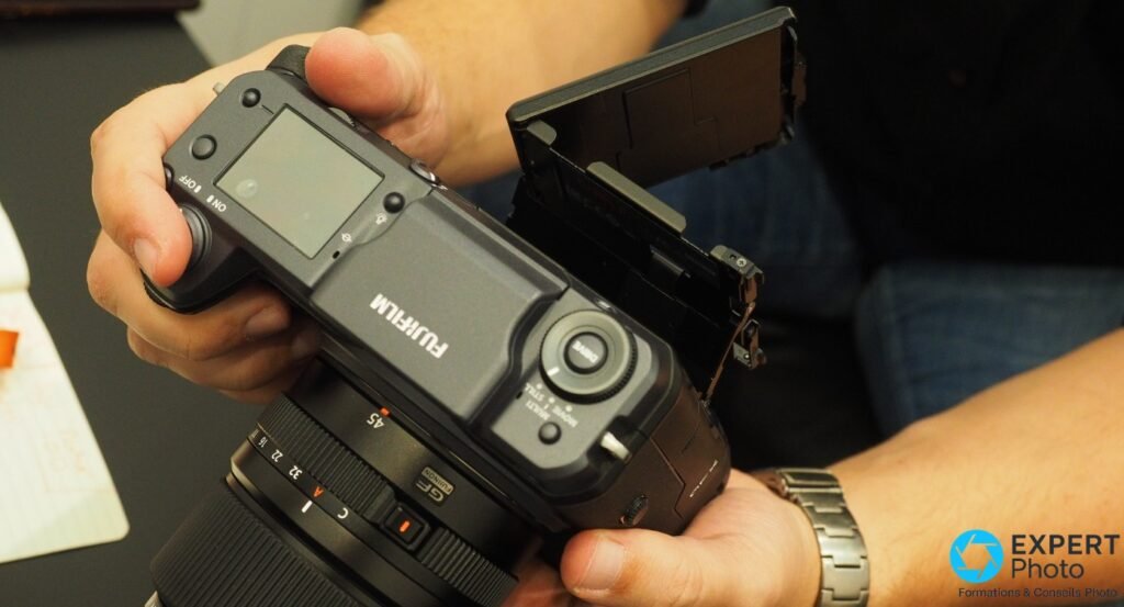 Fujifilm GFX 100 tenu à deux mains, écran arrière inclinable ouvert à 90°, objectif GF monté, commandes arrière visibles