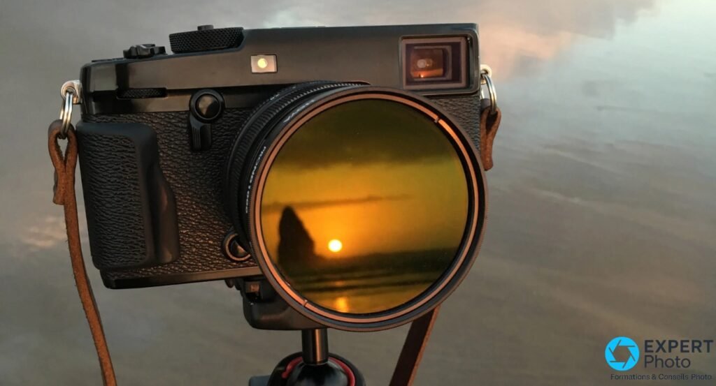 Boîtier Fujifilm X noir avec objectif XF 14mm et filtre circulaire monté, reflet coucher soleil visible dans le verre du filtre