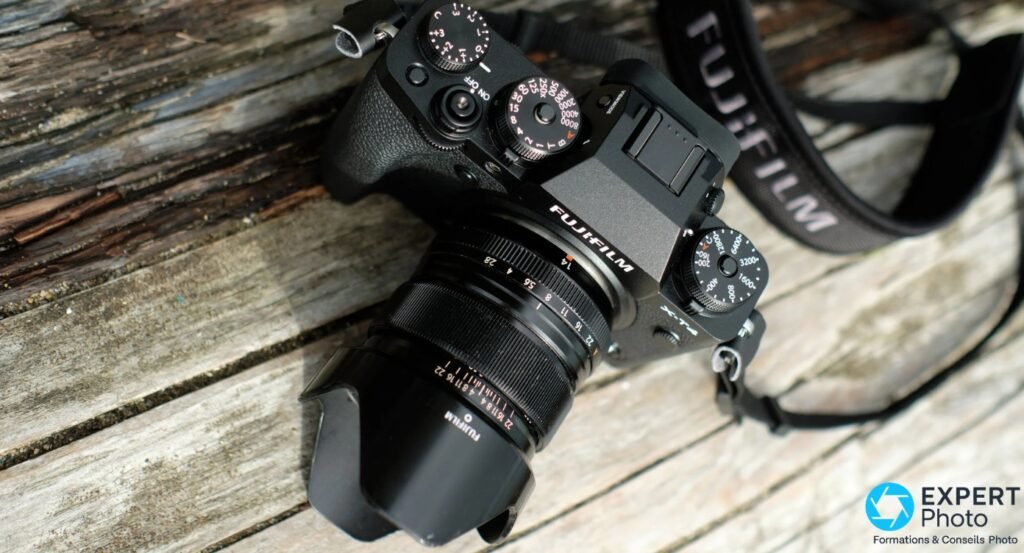 Boîtier Fujifilm X-T noir avec objectif XF 14mm f/2.8 R et pare-soleil vu du dessus, sangle Fujifilm textile visible