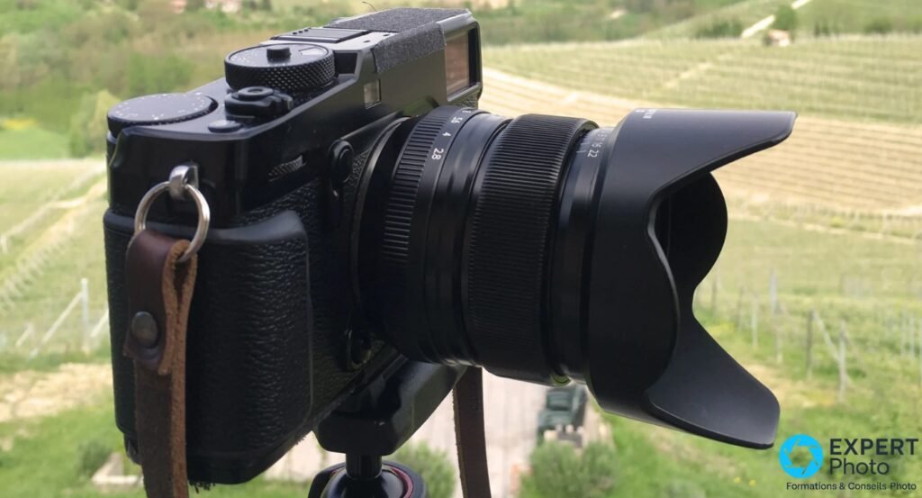 Boîtier hybride Fujifilm X noir vu de profil avec objectif XF 14mm f/2.8 R et pare-soleil pétales, en extérieur