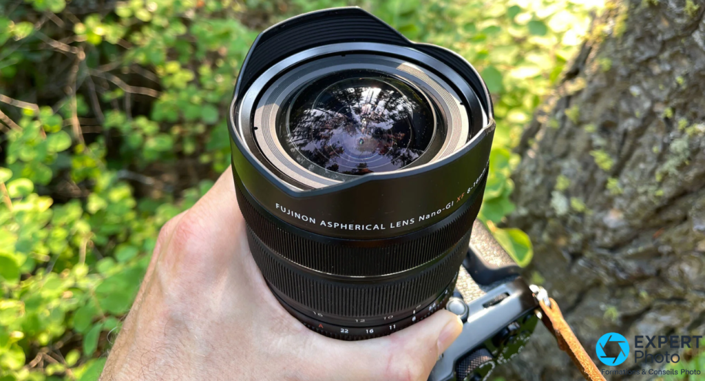 Fujifilm XF 8-16mm f/2.8 R LM WR tenu en main, vue plongeante sur l'élément avant bombé, bagues lisibles en dessous 