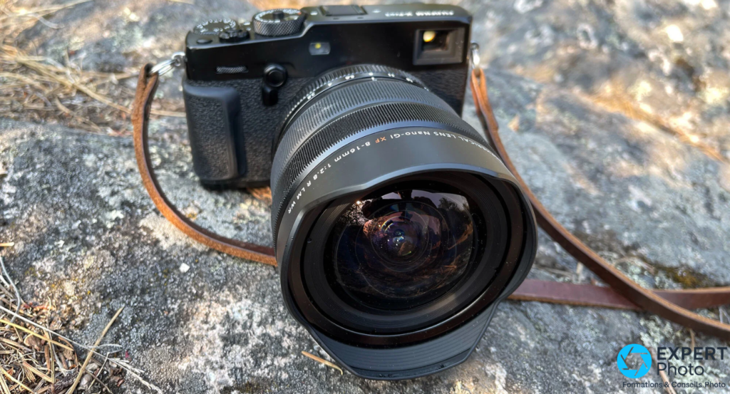  Fujifilm XF 8-16mm f/2.8 R LM WR monté sur boîtier Fujifilm noir sur roche, bonnette bombée face caméra, sangle marron