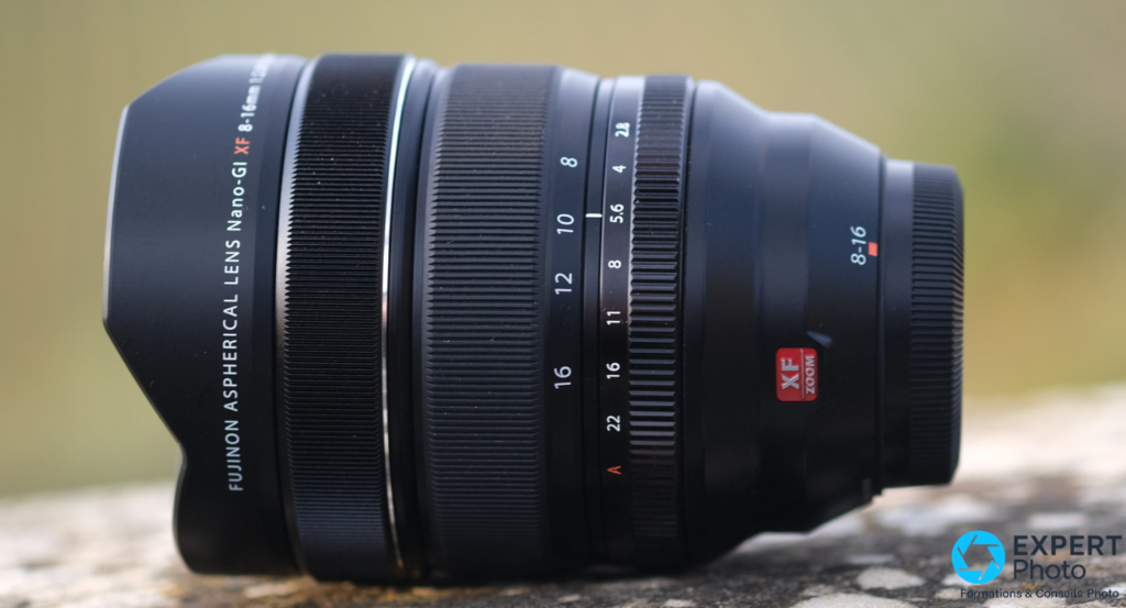Fujifilm XF 8-16mm f/2.8 R LM WR de profil sur pierre, bague de mise au point et badge XF Zoom rouge lisibles