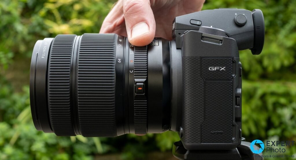 Fujinon GF 32-64mm F4 monté sur boîtier Fujifilm GFX, profil gauche strict, bague focale 64-32 et bouton orange visibles