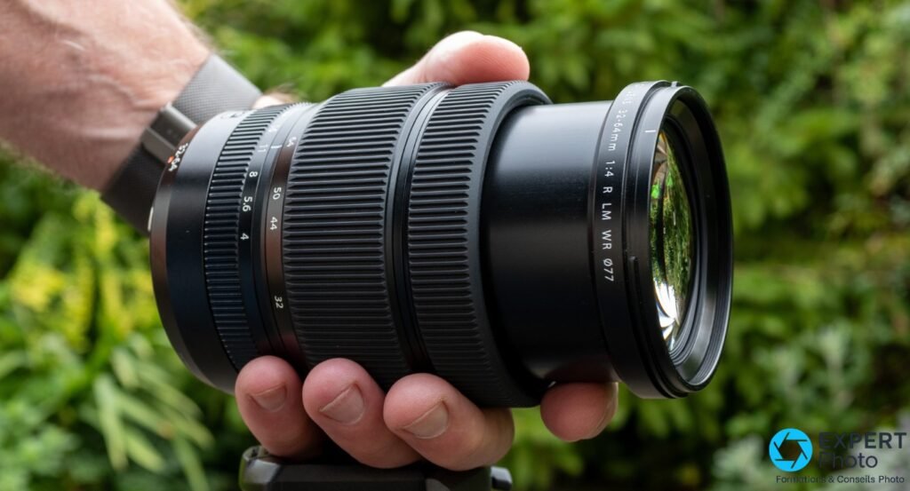 Fujinon GF 32-64mm F4 R LM WR tenu en main, profil droit, bagues focale 32-64mm et ouverture f/4 lisibles, filtre ⌀77