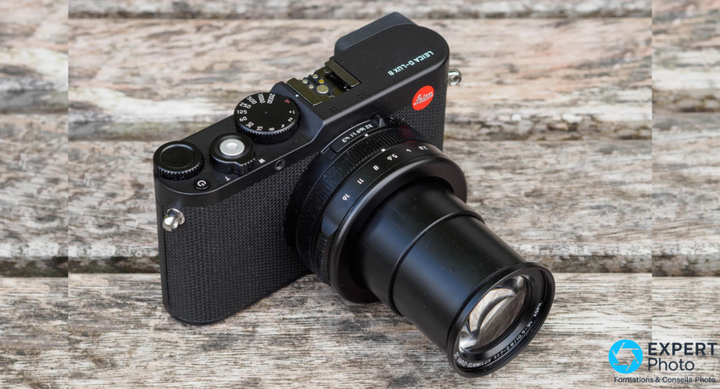 Leica D-Lux 8 noir 3/4 arrière, zoom Vario-Summilux étendu, molette ISO/vitesse et logo Leica rouge visibles