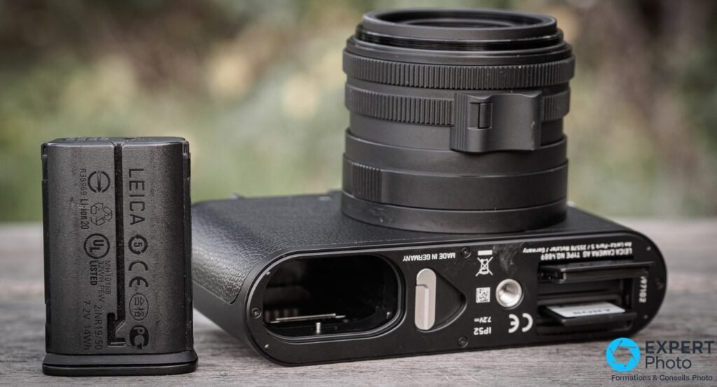 Dessous du Leica Q2 Monochrom ouvert avec batterie Leica extraite, marquage IP52 et slot carte mémoire visibles.