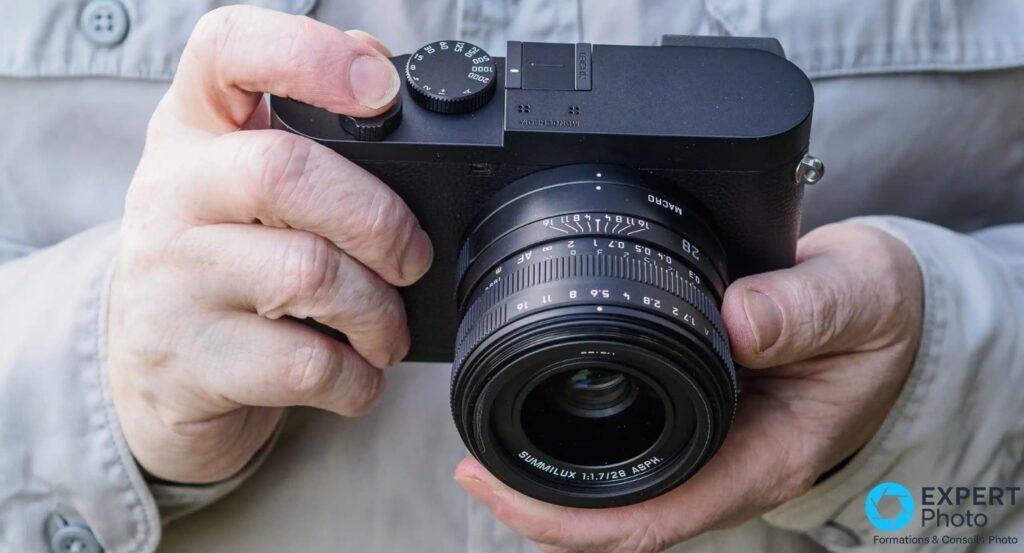 Leica Q2 Monochrom tenu en mains, inscription MONOCHROM visible sur la plaque, objectif Summilux 28 mm face caméra.