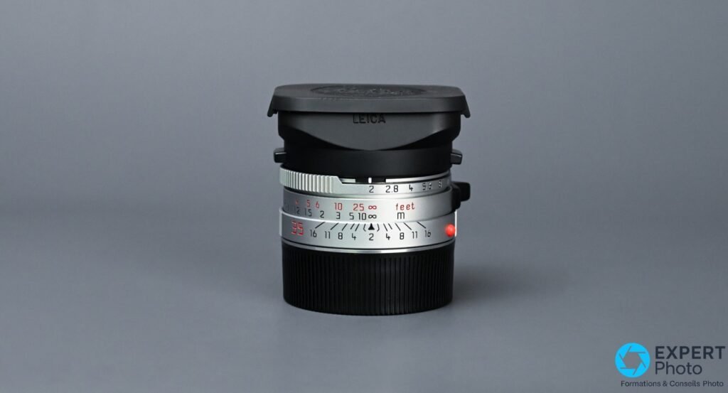  Leica Summicron-M 35mm f/2 IV chrome, bouchon avant noir gravé LEICA posé sur la face, bagues de distance et diaphragme visibles 