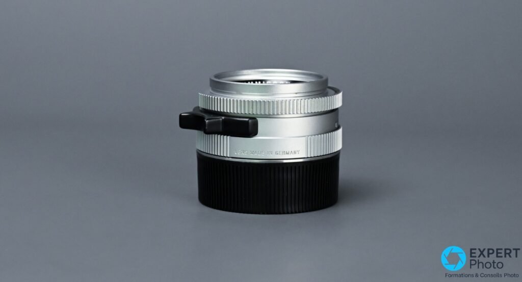 Leica Summicron-M 35mm f/2 IV chrome, vue 3/4 arrière gauche, inscription LENS MADE IN GERMANY sur la bague de monture, patte de mise au point visible
