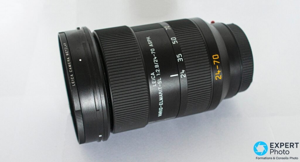  Leica Vario-Elmarit-SL 24-70mm f/2.8 ASPH posé à plat, vue 3/4 arrière, baïonnette L-Mount et repère rouge visibles