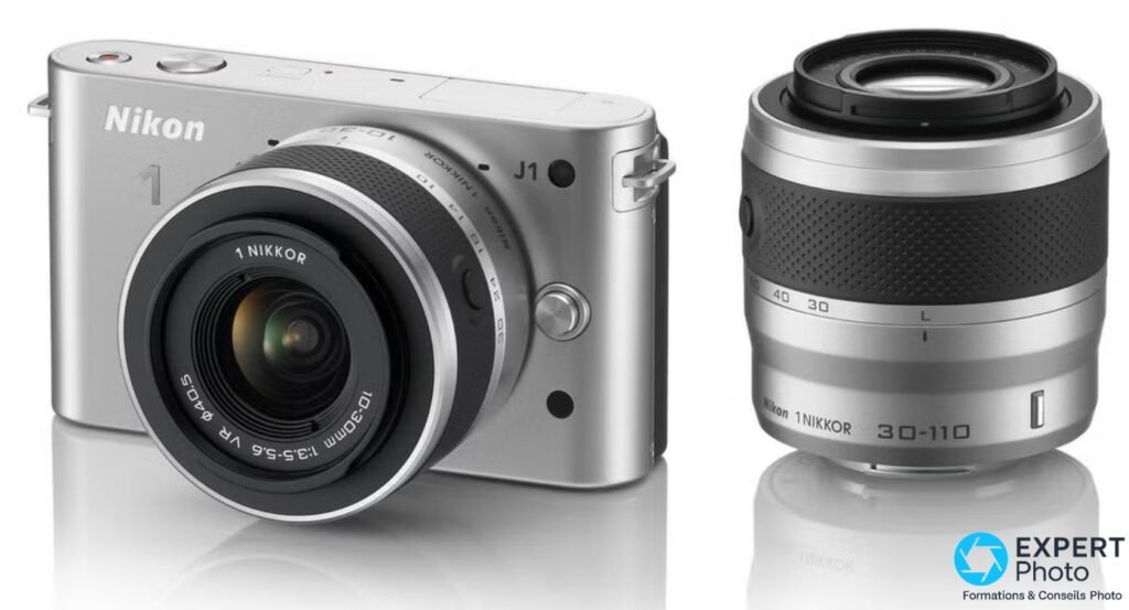 Nikon 1 J1 argenté équipé du 1 NIKKOR 10-30mm, zoom 30-110mm posé à droite, fond blanc
