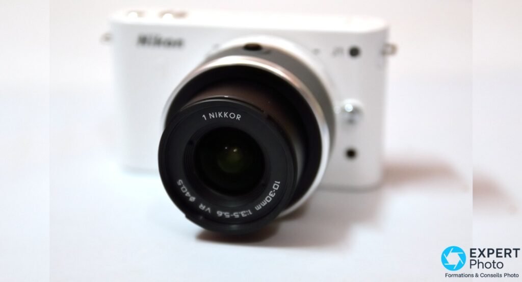 Gros plan du zoom 1 NIKKOR 10-30mm f/3.5-5.6 VR sur Nikon 1 J1 blanc, boîtier flou en arrière-plan