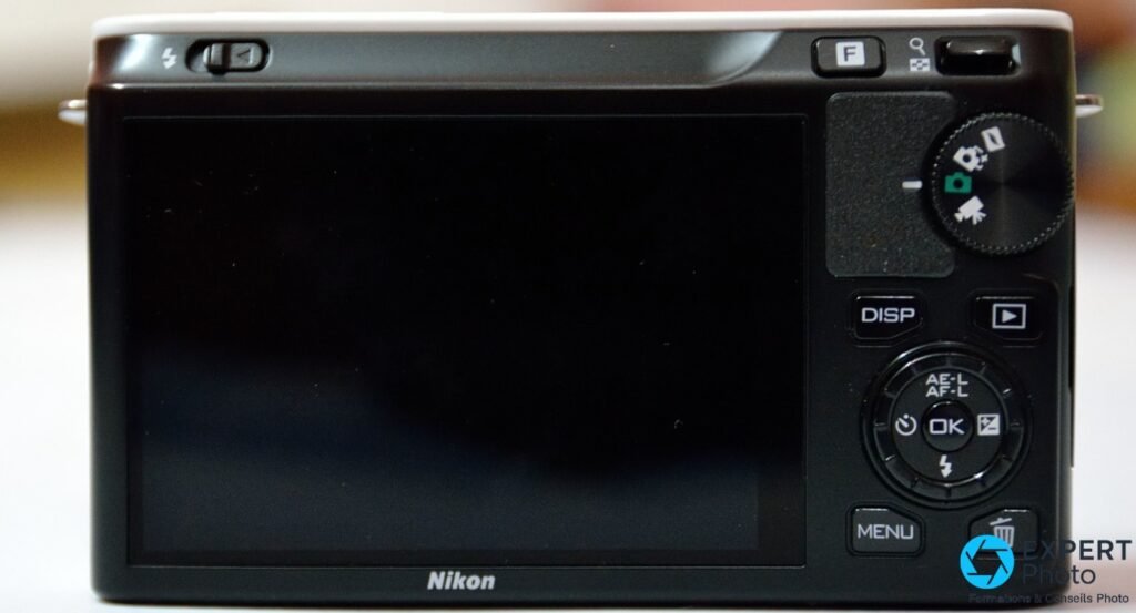 Face arrière Nikon 1 J1, écran LCD éteint, boutons DISP, MENU, AE-L/AF-L, OK et molette de sélection de modes visibles