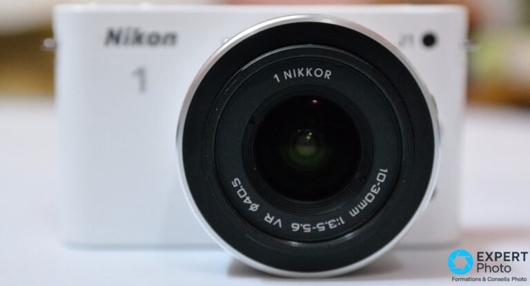 Nikon 1 J1 d’occasion : ce qu’il est vraiment en 2026 Gros plan frontal du zoom 1 NIKKOR 10-30mm f/3.5-5.6 VR monté sur Nikon 1 J1 blanc, lentille nette